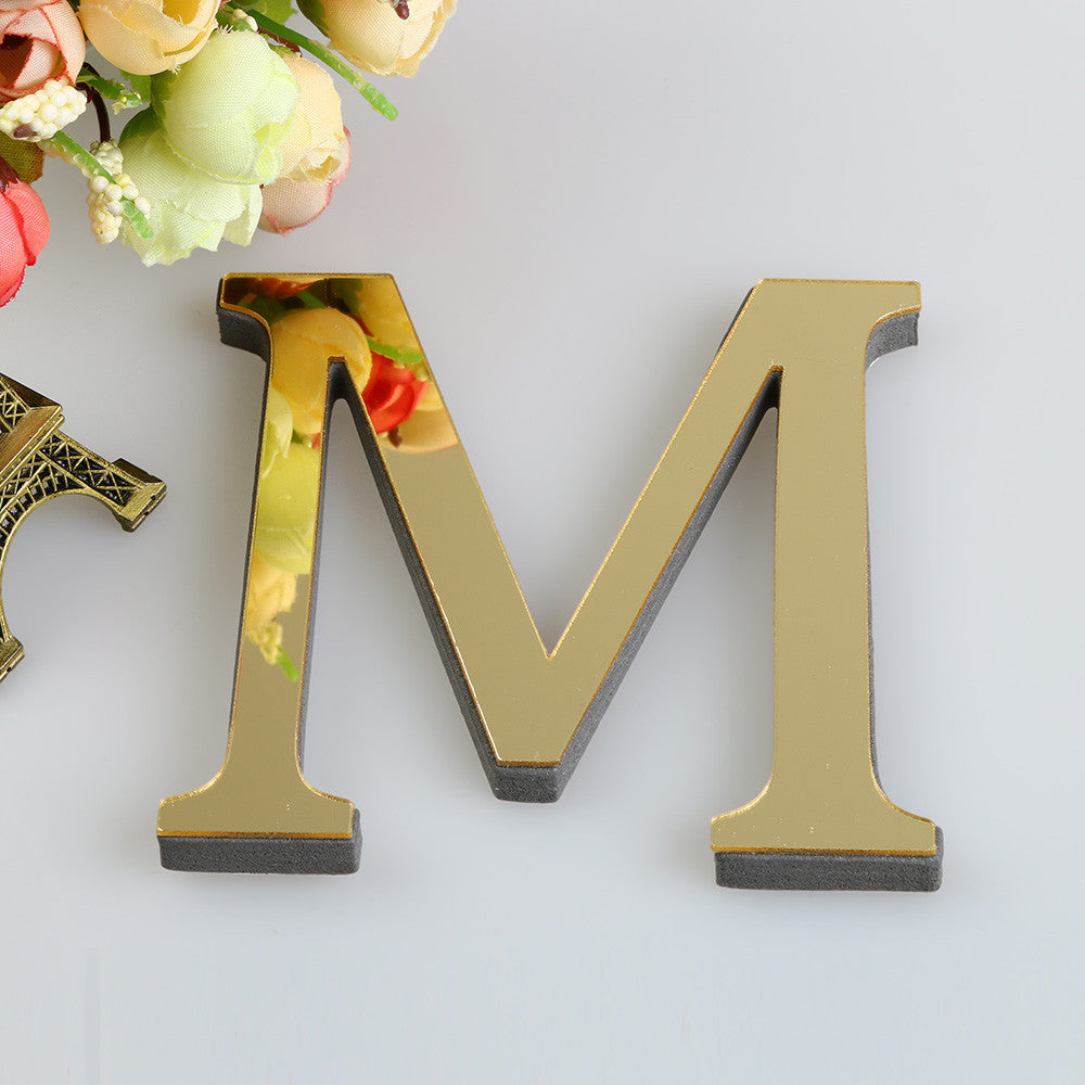 A set of three 3D golden letter mirror wall decals, M, displayed against a white background with floral elements.