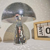 A silver, mushroom-shaped disco ball decoration with a faceted glass base sits on a white surface.
