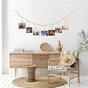 A wooden photo display garland hangs on a white wall above a light wood cabinet and a woven rug.