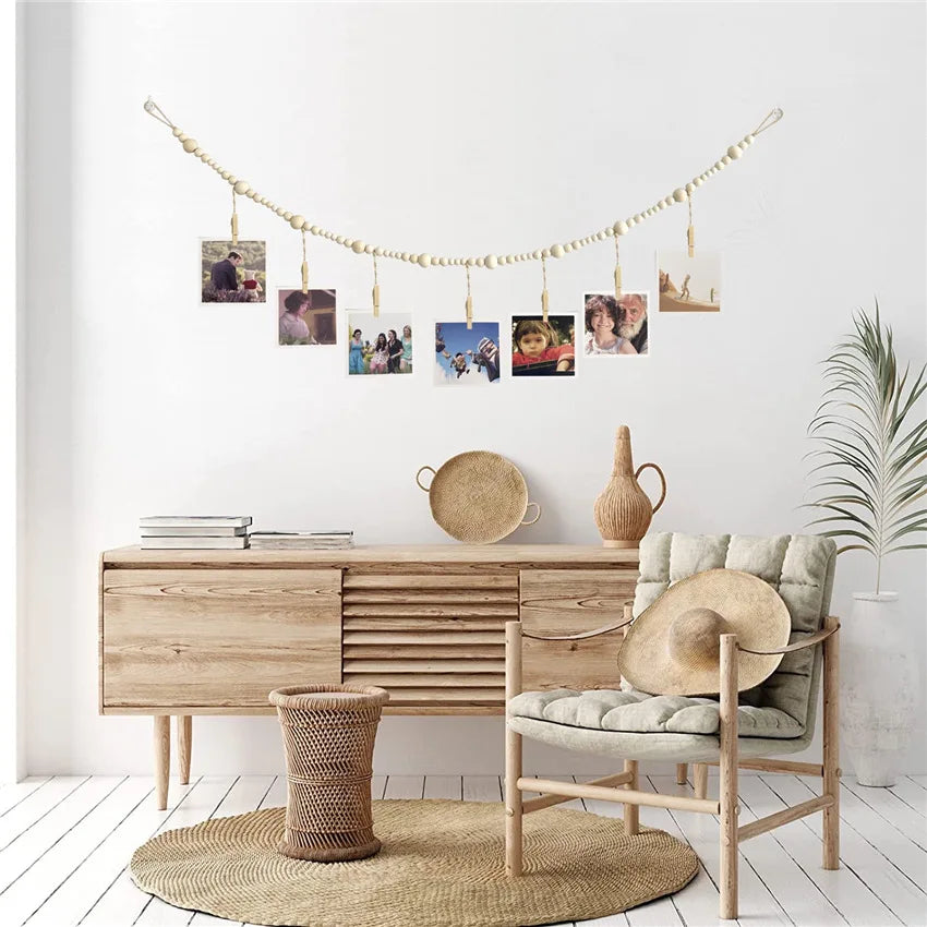 A wooden photo display garland hangs on a white wall above a light wood cabinet and a woven rug.