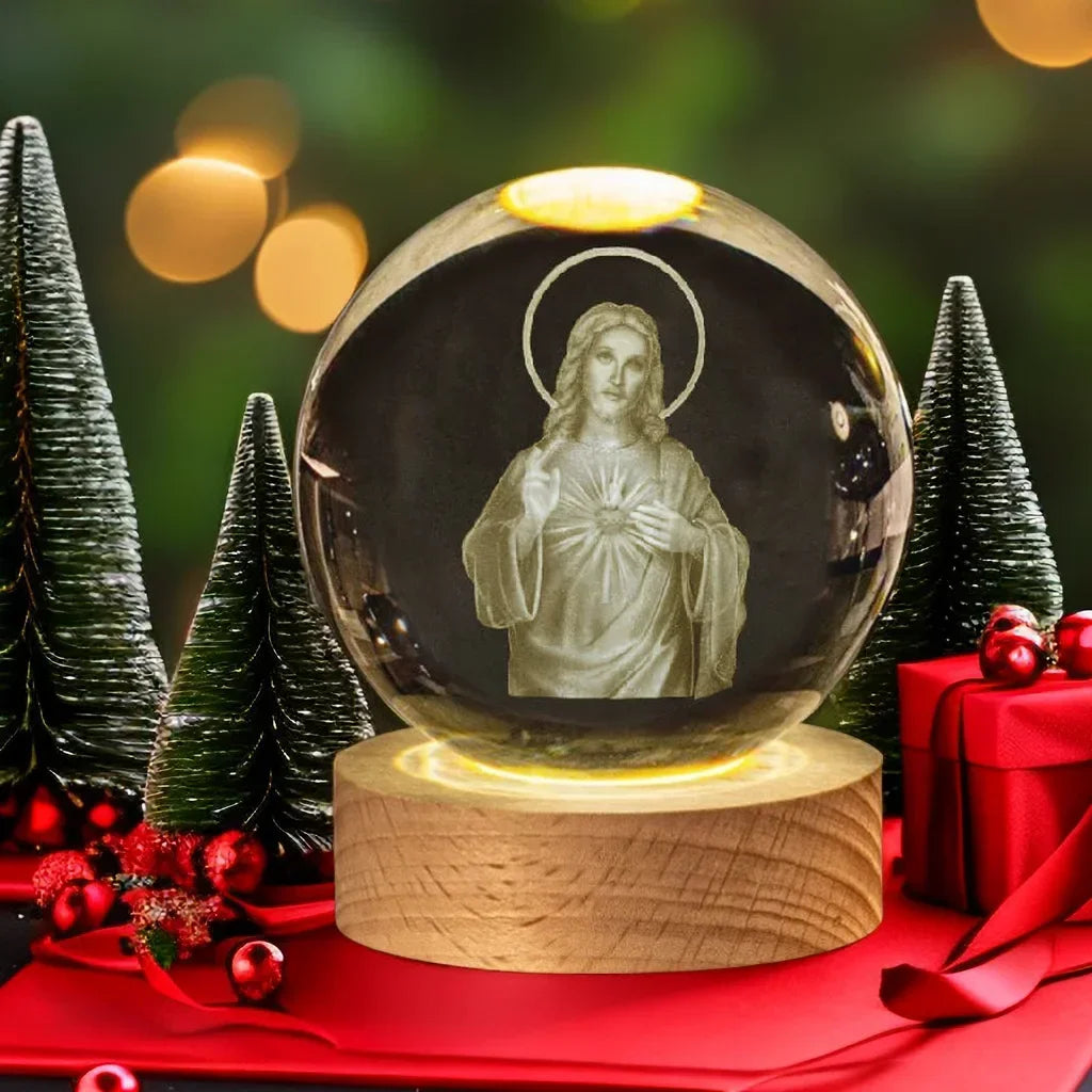 A glass crystal ball night light featuring a figure of Jesus, set on a wooden base and surrounded by green pine trees.