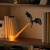 A dark dragon silhouette with glowing orange flame illuminates a wooden bookshelf nook.