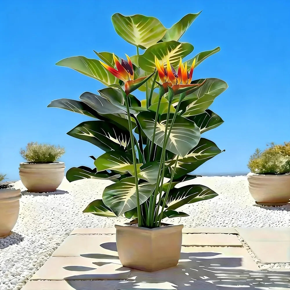 A vibrant artificial Bird of Paradise plant with large green leaves and orange-red flowers in a terracotta pot against a brig