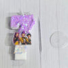A birthday candle featuring a purple glitter design and an acrylic topper with three character figures.