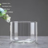 A clear glass cylindrical vase with a wide opening, displayed on a gray surface.