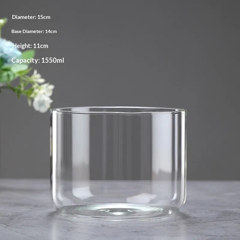 A clear glass cylindrical vase with a wide opening, displayed on a gray surface.