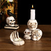 A white resin skull candle holder decoration with a lit candle and a black silhouette of a bird on a wooden surface.