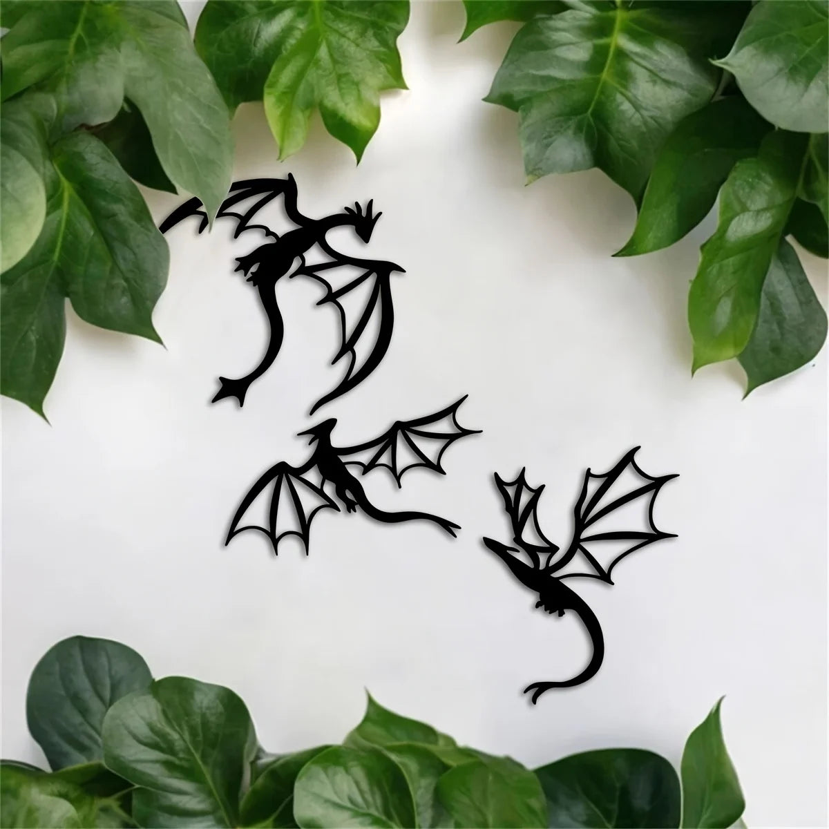 A set of three black dragon metal wall art panels displayed on a white background surrounded by green leaves.