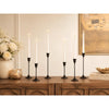 A set of three tall white taper candles in vintage metal holders displayed on a wooden table.