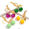Gold-toned resin cherry pendant keychain featuring pink, green, and yellow fruit shapes.