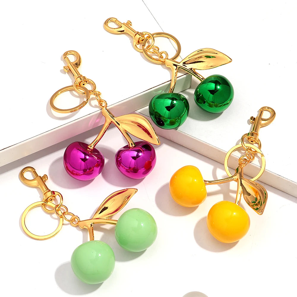 Gold-toned resin cherry pendant keychain featuring pink, green, and yellow fruit shapes.