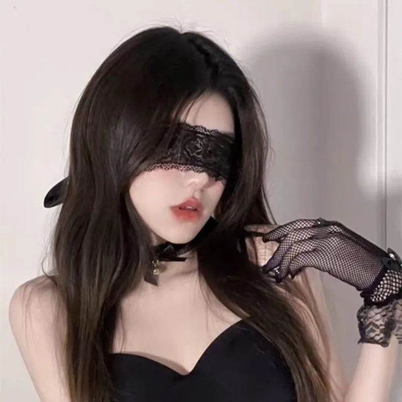 A woman with long dark hair wearing a black lace masquerade eye mask and black sheer gloves.