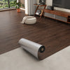 A close-up view of dark brown wood grain self-adhesive flooring film installed on a light floor.