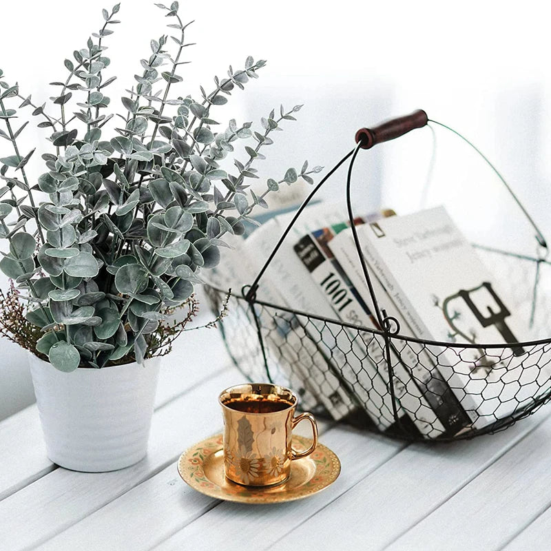 A potted plant with silvery-green eucalyptus leaves sits next to a gold cup on a white wooden surface.