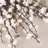 A branch of artificial white plum blossoms on dark branches against a light background.