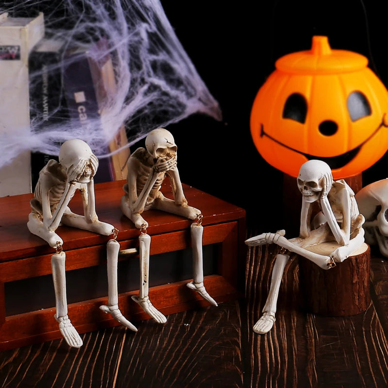 A set of three white resin skeleton skull figurines displayed on a wooden surface.