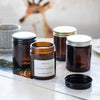 Two amber glass jars with silver lids and labels sit on a white surface.