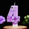 A purple glitter number candle shaped like the number 4 decorated with a small purple flower on a wooden surface.