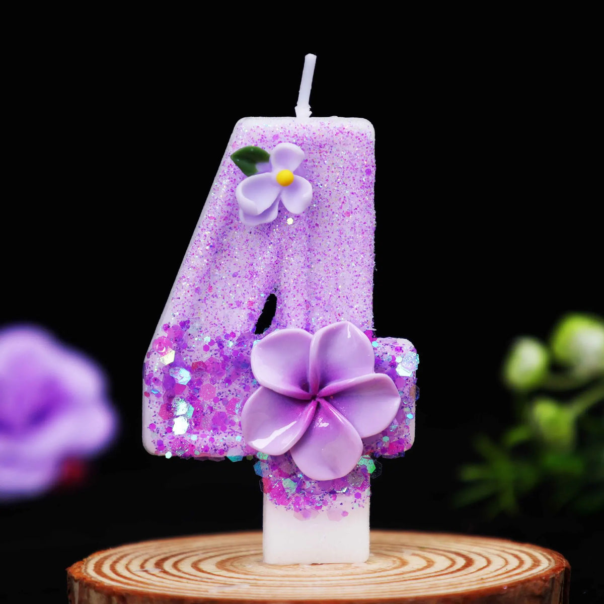 A purple glitter number candle shaped like the number 4 decorated with a small purple flower on a wooden surface.