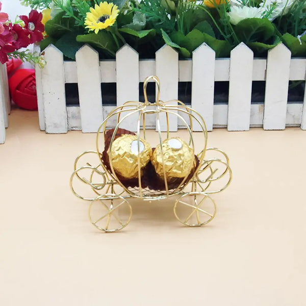 A golden pumpkin carriage candy box with gold wheels and wrapped treats displayed in front of greenery.