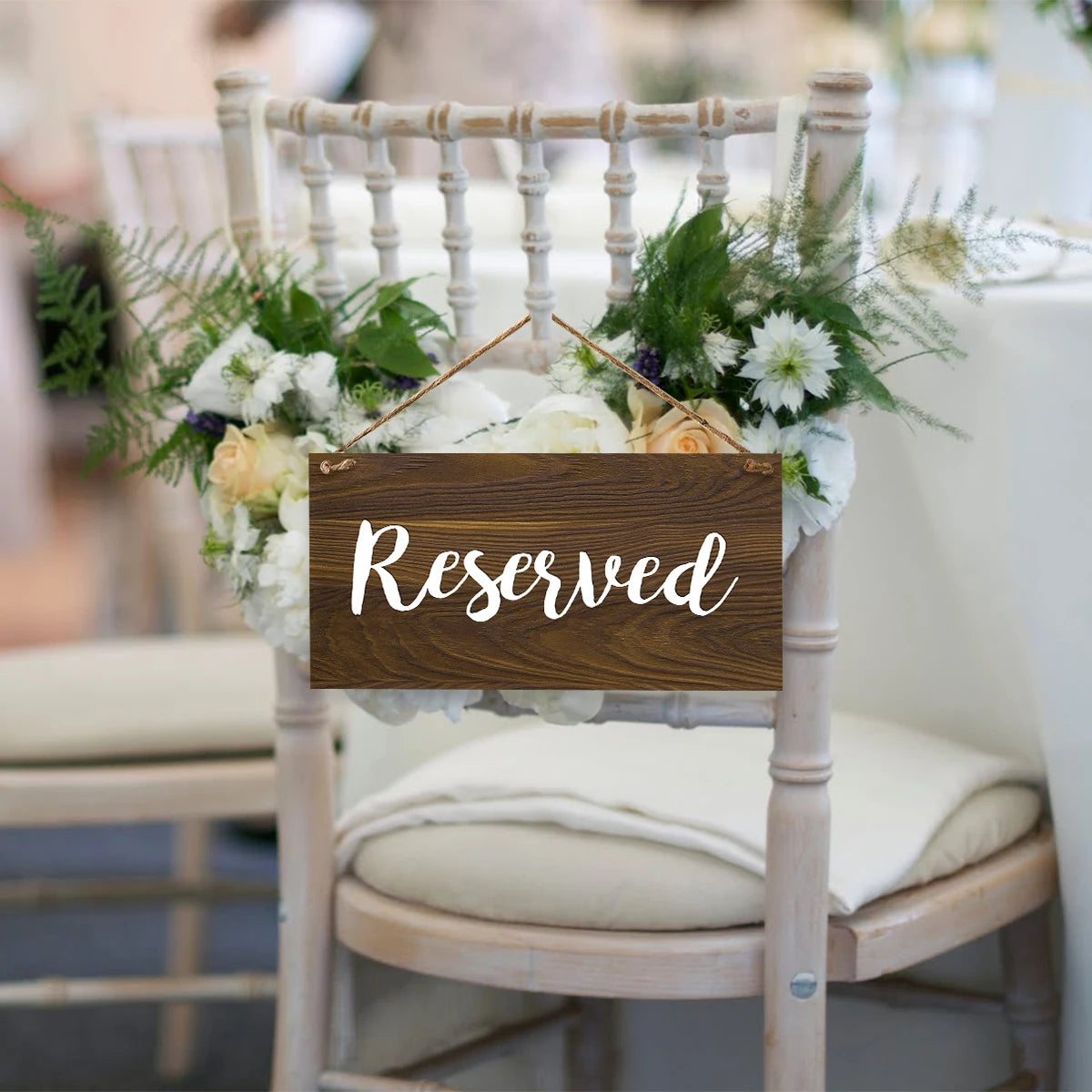 A rustic wooden reserved sign with greenery and white flowers is displayed on a light wooden chair.