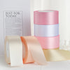 Un ensemble de rubans décoratifs en satin dans des tons de rose, pêche et crème sont exposés sur une surface blanche.