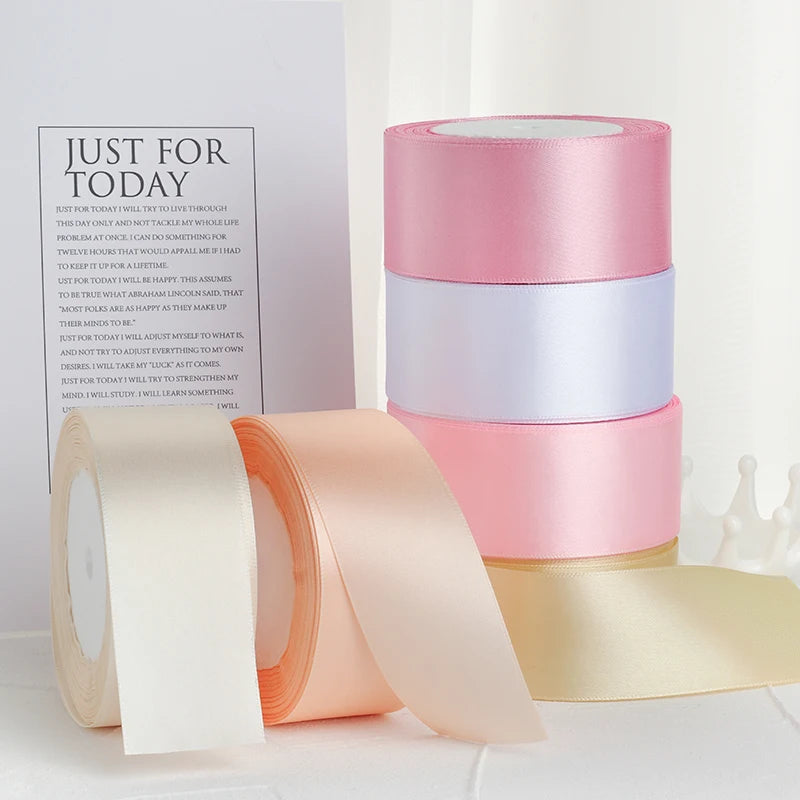 Un ensemble de rubans décoratifs en satin dans des tons de rose, pêche et crème sont exposés sur une surface blanche.