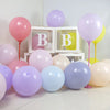 A collection of pastel rainbow latex balloons in pink, purple, yellow, and light blue are displayed on a white surface.