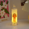 A clear glass votive candle with a flame-like LED light inside, featuring a small golden figure.