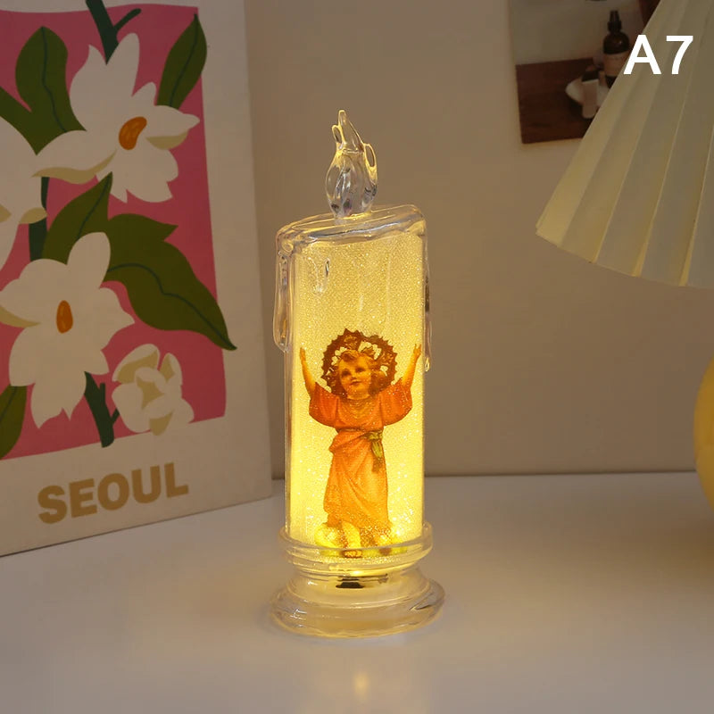A clear glass votive candle with a flame-like LED light inside, featuring a small golden figure.