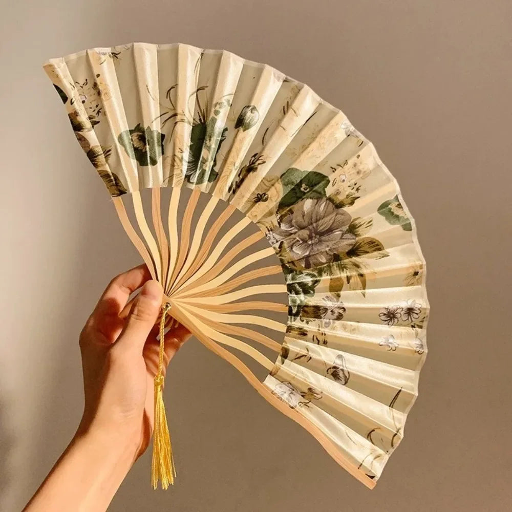 A hand holding a light beige folding fan with a leopard print design and black handle.