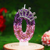 Glitter number zero birthday candle with rhinestone crown cake topper on a wooden surface.