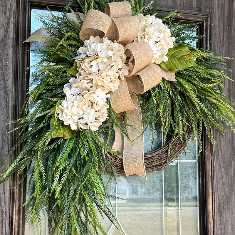 A rustic wreath made of green foliage and white hydrangeas tied with natural brown ribbon, displayed on a door.