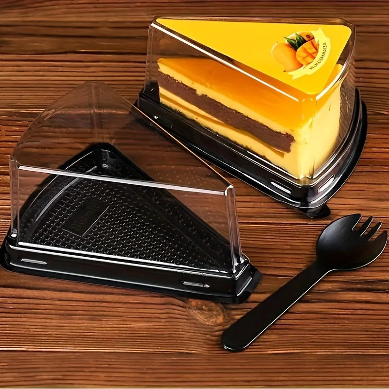 A slice of yellow cheesecake in a clear plastic container is shown next to a black serving plate and a fork on a wooden surfa