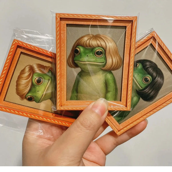 A hand holds an orange wooden photo frame featuring a realistic green frog illustration.