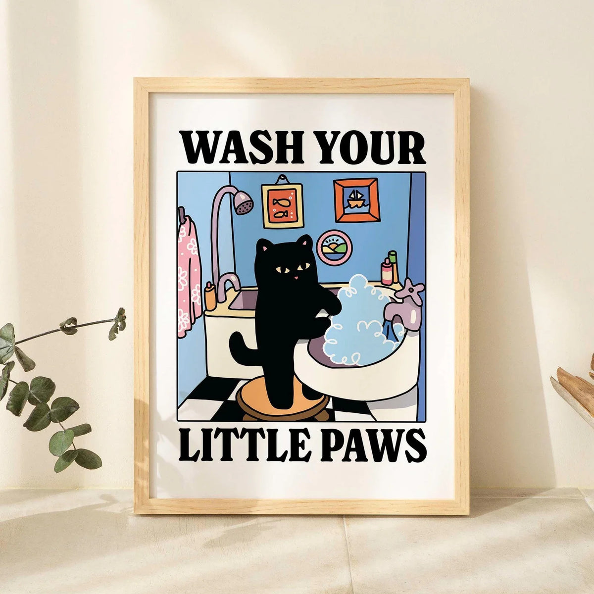 A framed poster featuring a cartoon black cat washing its paws in a bathtub, with the text Wash Your Little Paws.