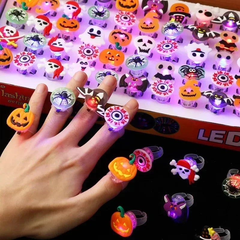 A hand holds a tray of Halloween glow rings featuring various spooky and cute faces, including pumpkins and ghosts.