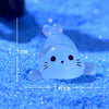 A translucent blue glow in the dark resin sea animal figurine resting on a blue glitter surface.