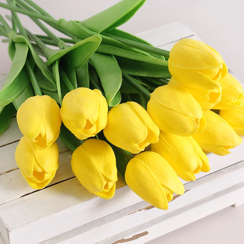 A bouquet of bright yellow artificial tulip flowers with green stems arranged on a white surface.