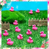 A collection of pink miniature resin flamingo duck figurines scattered across vibrant green grass.