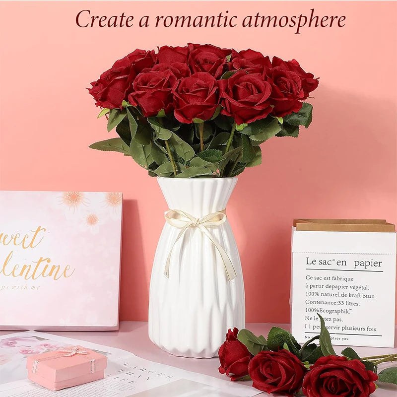 A bouquet of deep red artificial silk roses in a white vase on a pink background.