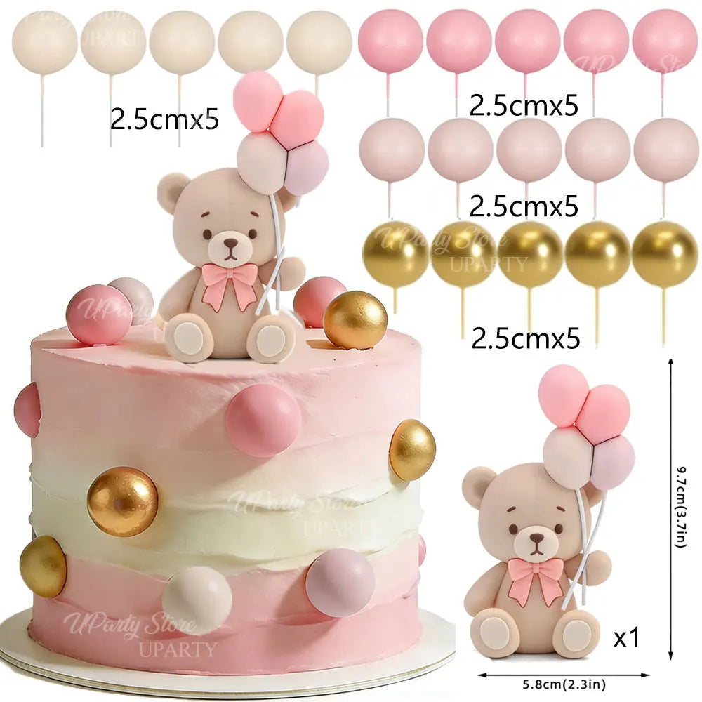 A tiered pink cake decorated with bear figures and round ball toppers in pink and gold colors.