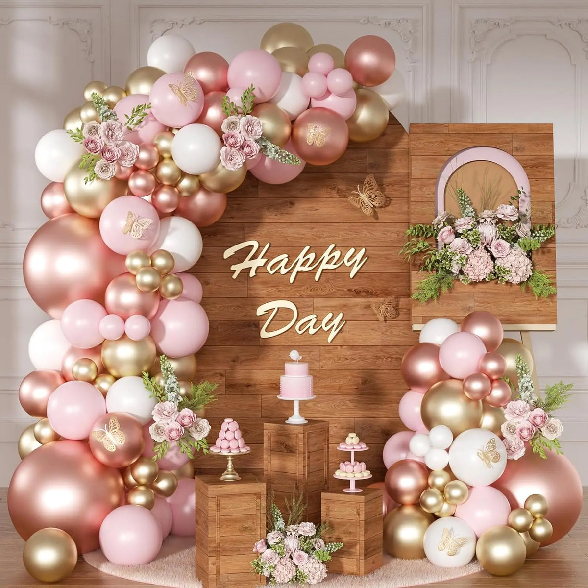 A pink and gold latex balloon garland featuring roses and macarons arranged on a wooden background.
