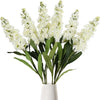 A bouquet of artificial white delphinium flowers with green leaves in a white vase.