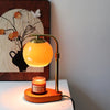 A golden aromatherapy wax melting lamp with a warm glow sits on a white surface next to a framed botanical print.