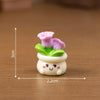 A small resin charm depicting a pink rose growing from a green leaf on a white base.