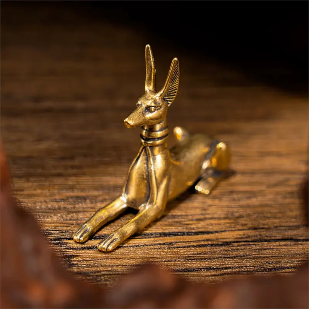 A vintage brass Pharaoh hound statue with long ears resting on a wooden surface.