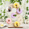 A wooden number display stand shaped like the number 3 holds various colorful frosted donuts.