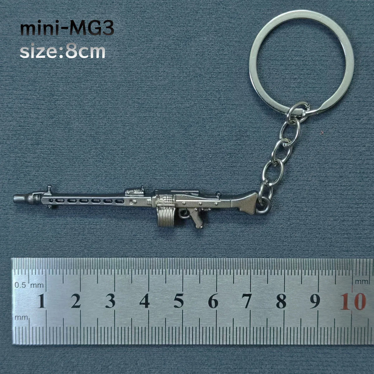 A silver miniature MG3 alloy gun model keychain with a metal ring attached, shown next to a ruler.