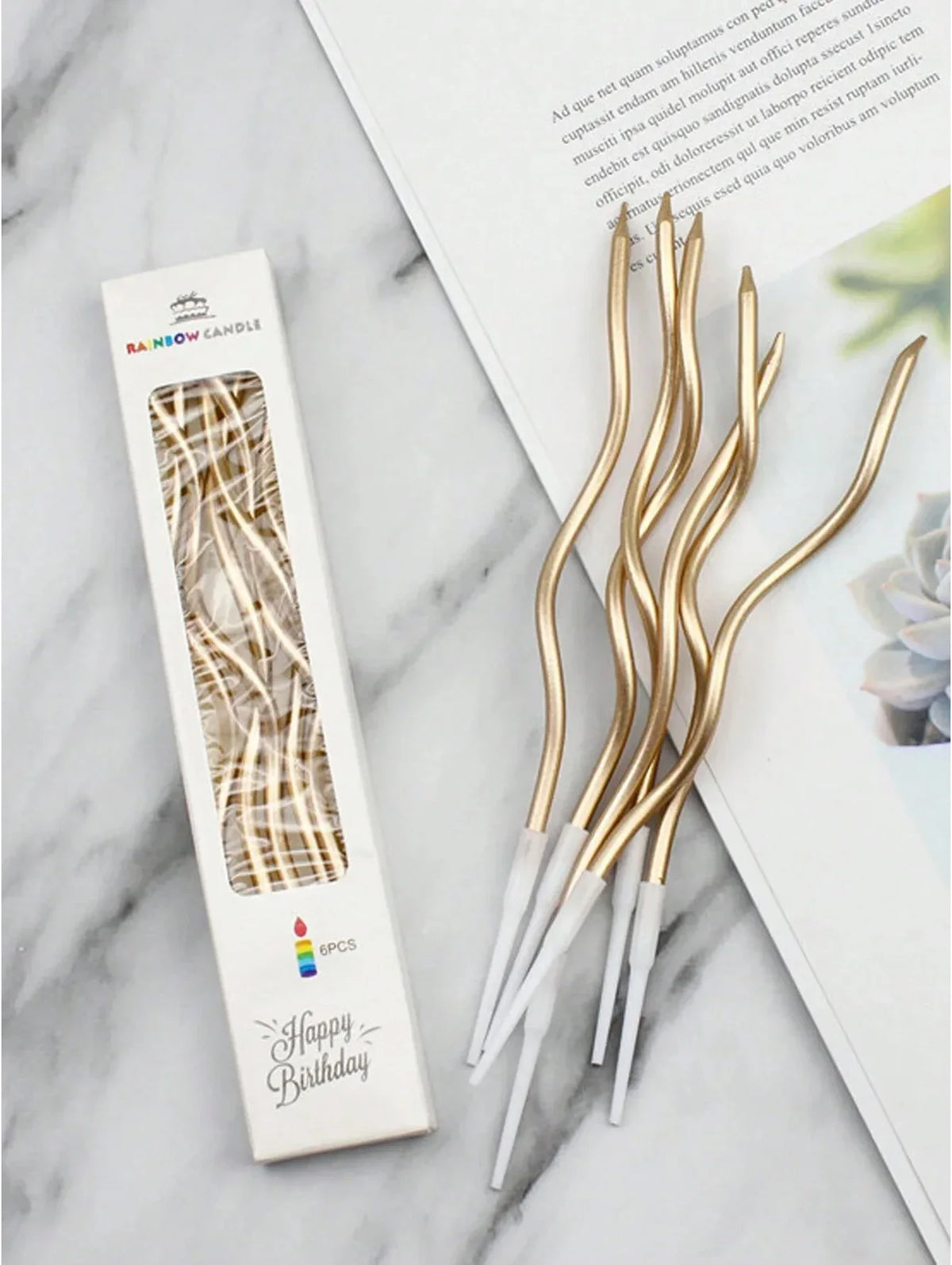 A set of six gold curved decorative birthday candles in a white box next to a page of text.